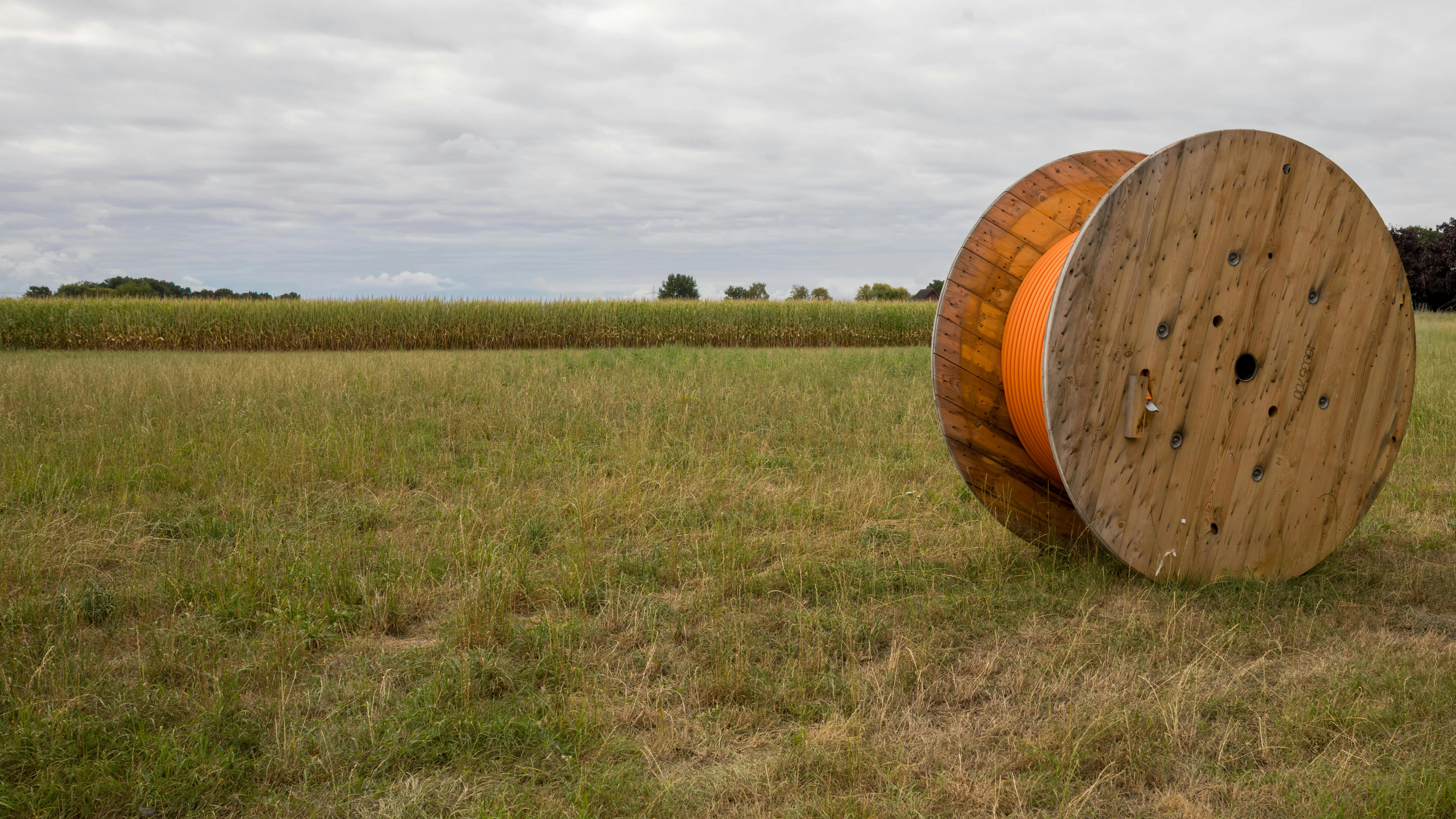 Large wooden spool of orange cable laying in grassy field